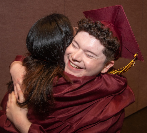 young man in grad cap hugging another grad
