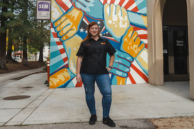 woman in Auto Tech shirt standing in front of Veteran's Mural