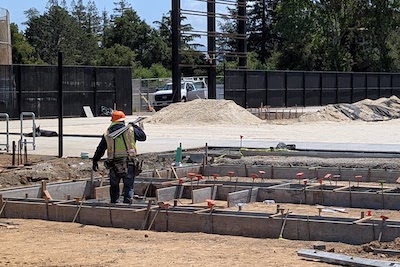 construction site with worker carrying metal pipes over shoulder