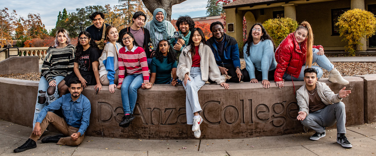 students seated in front of De Anza sign