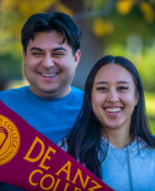 two smiling students with De Anza pennant