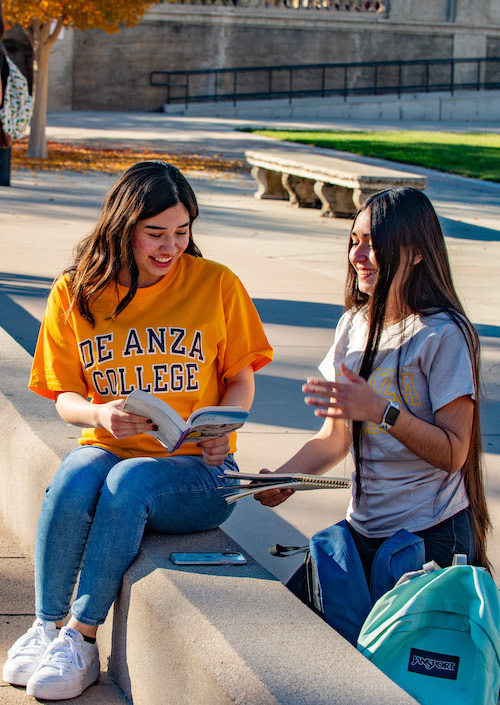 two young women talking outside, one with yellow De Anza shirt